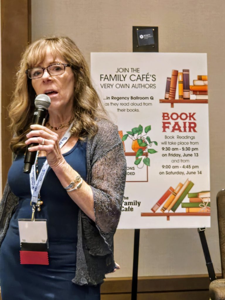 Author with a microphone speaking in front of a Book Fair sign