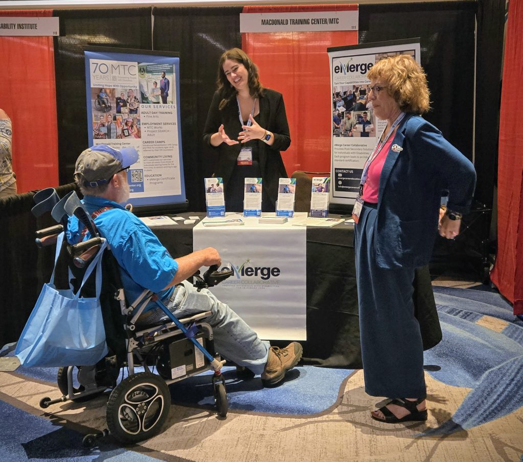 Exhibitor at their booth describing their product to an attendee in a wheelchair