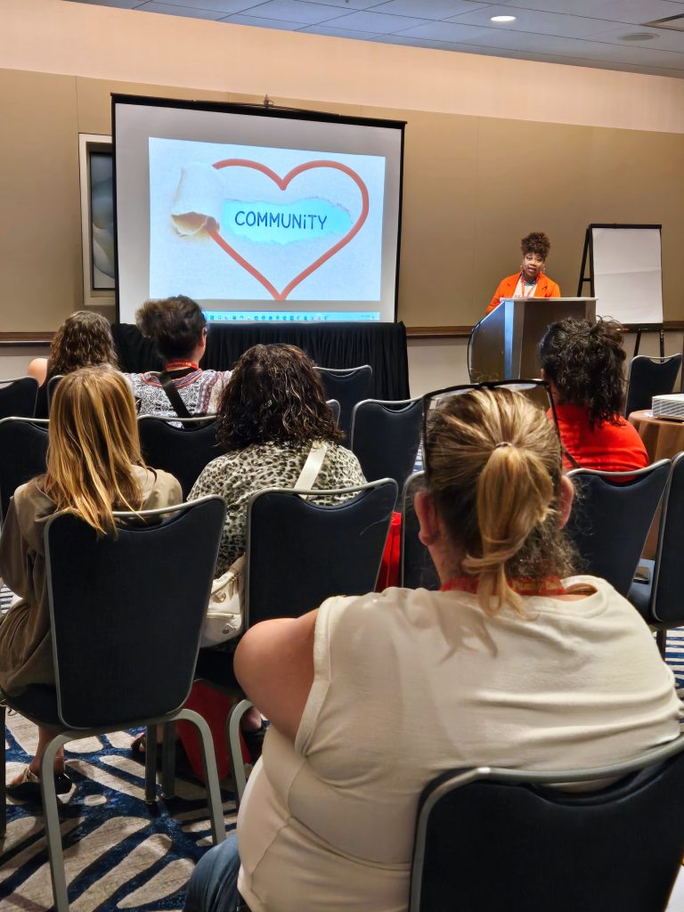 woman delivering a presentation with a slide that says "community" in a heart projected on the screen