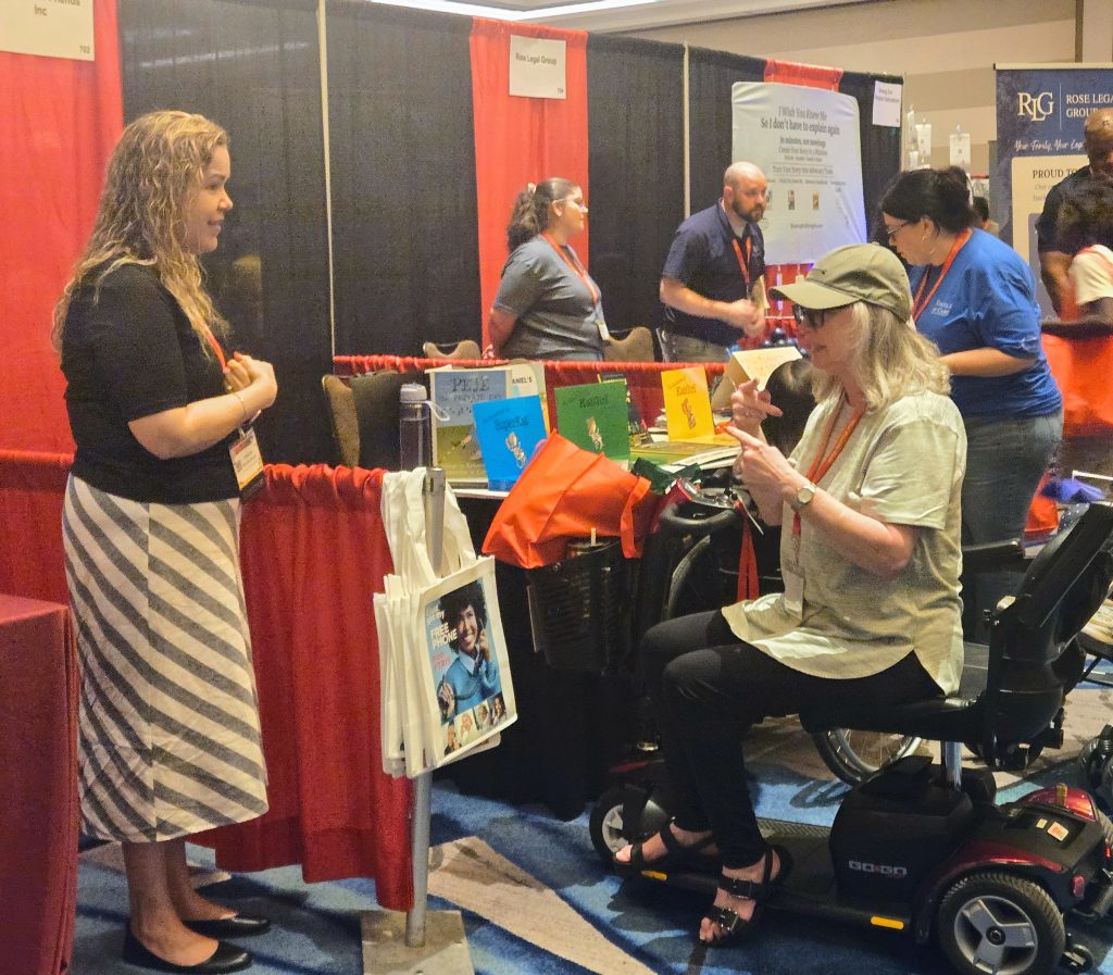 Exhibitor at their booth talking to an attendee in a scooter