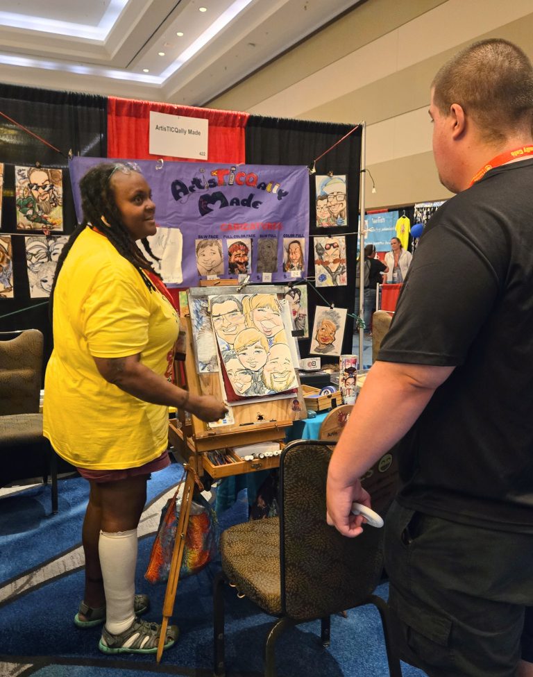 Micro-enterprise participant in a yellow shirt sharing their art at their booth